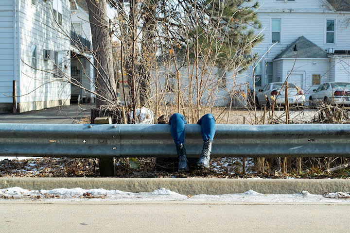 legs hanging over guardrail along a road with houses in the background