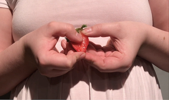 close up of a female's hands holding a sliced strawberry