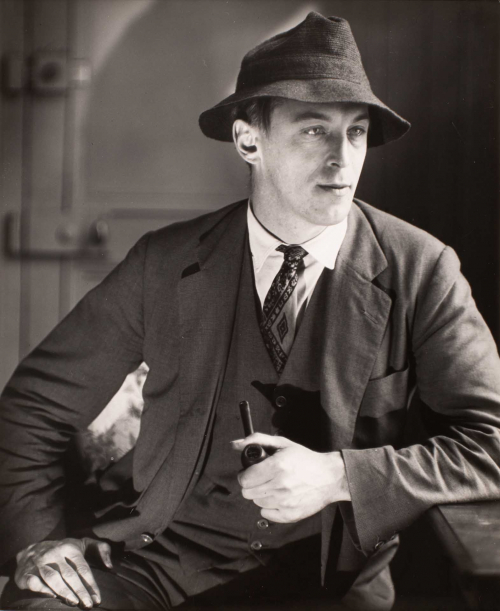 Man seated; body frontal; head turned 3/4 profile; wearing three piece suit, tie, hat and holds pipe in left hand. 