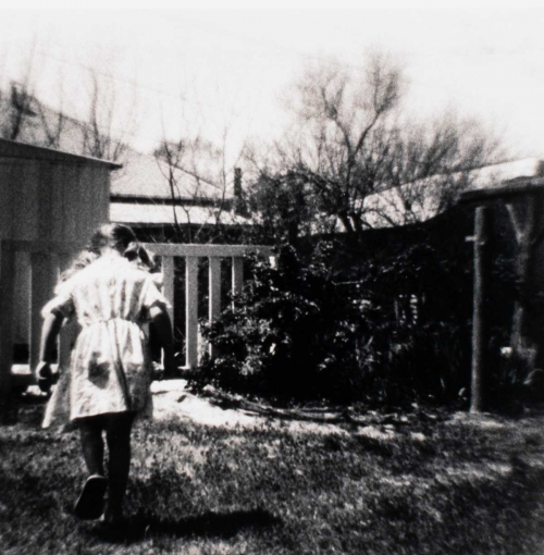 A black and white image in a residential landscape with a young girl to the far left who walks away from the viewer.