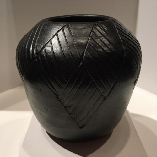 A small shiny black pot with diagonal incisions forming five diamond patterns from the rim to the mid-body of the vessel