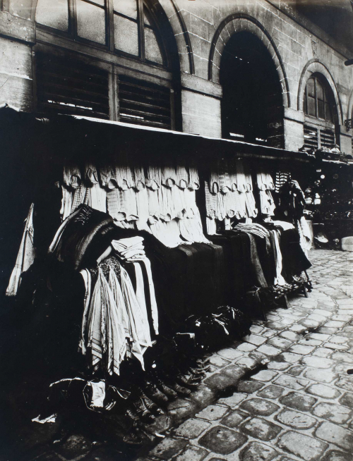 Crowded clothing kiosk on street in front of brick building.
