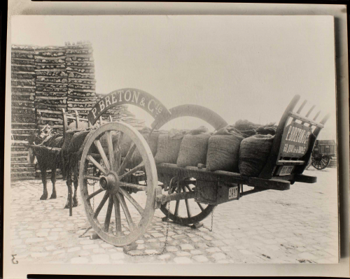 Horse pulling 'P. Breton at Cie' wagon Lumber stacks on left side.  Partial wagon seen to right behind center wagon