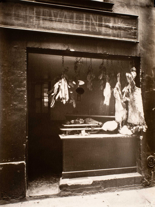 Interior of butcher shop viewed from the street.  Butchering table meat hanging above.