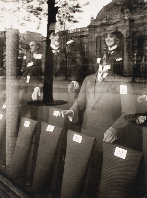 Mannequins modeling three-piece suits in store front.  A tree and buildings are reflected in store window.