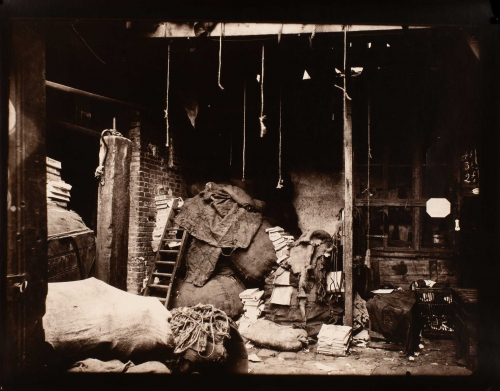 interior of dark, disheveled room.  Ropes hung from ceiling beams, burlap bags and stacks of paper