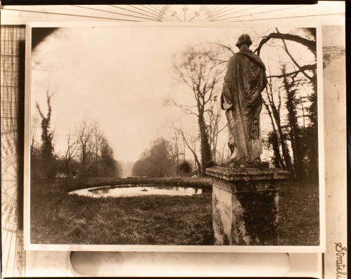 View of small pond below center, bare trees on both sides, and draped statue seen from behind on right.