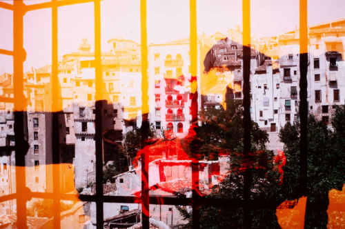 View of rear of apartments through barred window or balcony.  Image is red in center, yellow at top and left, and orange in LR