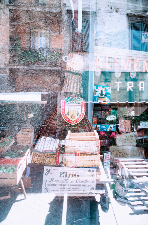 Store interior seen through glass and reflection or montage of Italian Street market and old buildings.