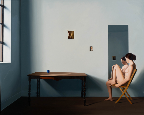 gray wall and two small pictures taped on, a table bare except for a blue mug, and a nude female seated in front of a mirror