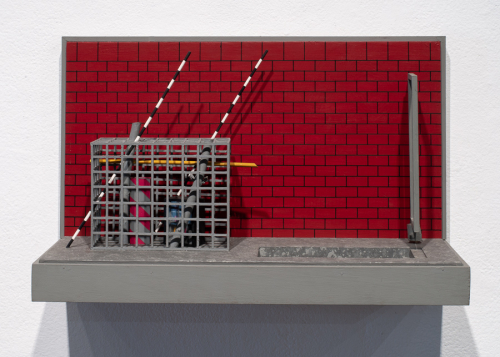 rectangular hanging relief sculpture depicting a red brick wall and a foreground pit with steps beside a rectangular cage