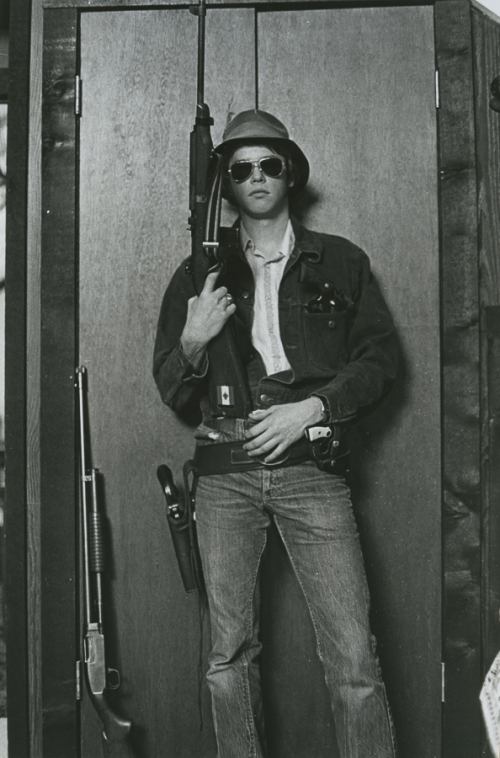 Man with sunglasses standing with a rifle