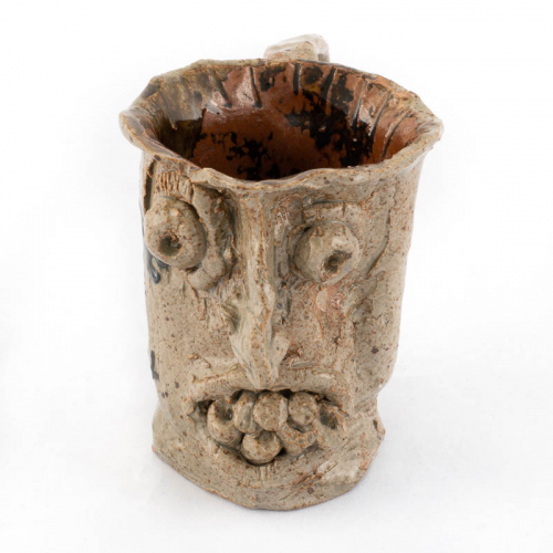 A brown "face jar" mug with large handle. The artist has written on the side "Terrance needed a dentist."