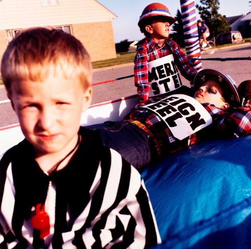 Three young boys role-playing as boxers and referee.  American steel vs. Foreign Steel.  Close-up of one boy along left edge.