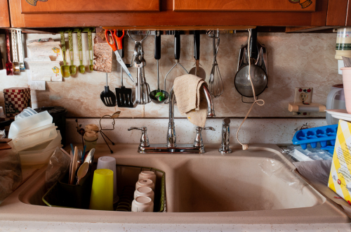 complex composition featuring a kitchen sink, cooking utensils, and plastic containers, all beneath a wooden cabinet