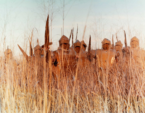 A full-color image with a low vantage point depicting soldiers with swords advancing through tall grasses.