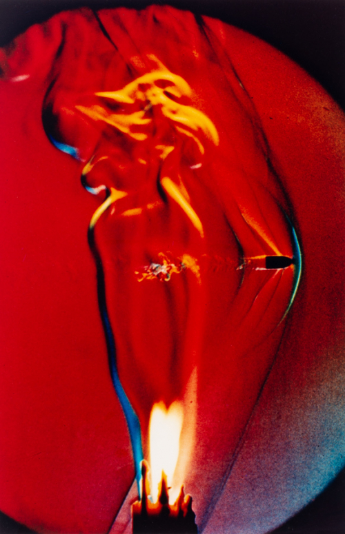 Photograph of a bullet piercing a deep red flame.