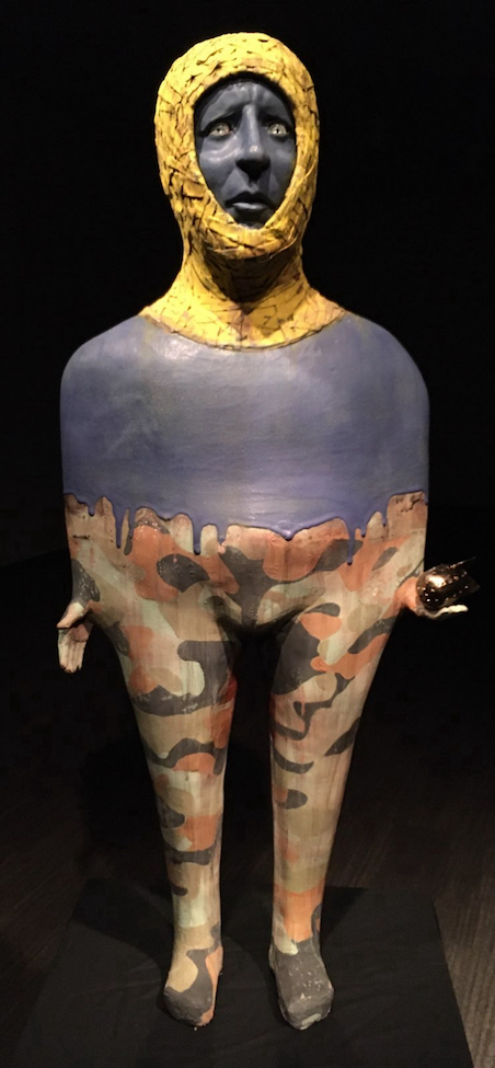 Front: A free-standing figure with a textured yellow hood, a blue face and torso, and a camouflaged waist and legs