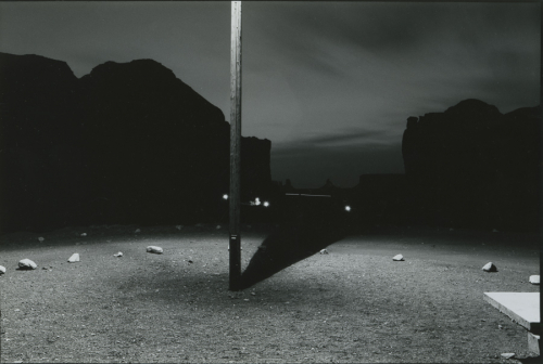 Nighttime view of a lamppost, casting shadows on the ground and large rocks