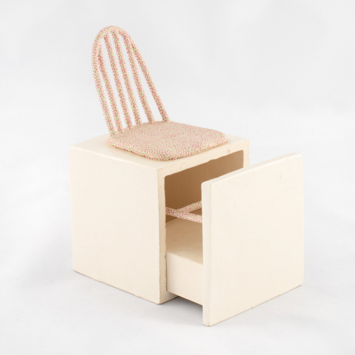 a white box with the seat and back of a pink and green dotted chair on top, a drawer pulls out revealing chair legs