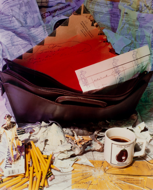 A briefcase filled with pieces of mail, a cup of coffee to right and a bunch of pencils, crumpled papers, broken glass on bottom