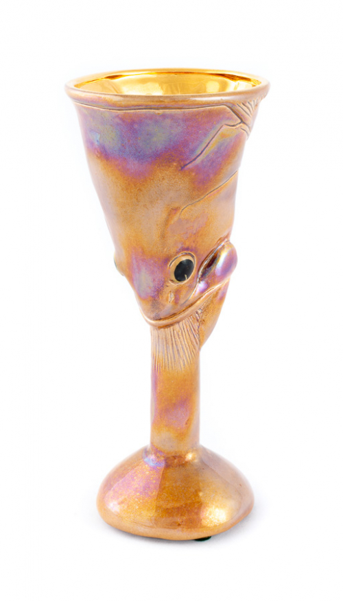A ceramic goblet, cup itself is the head of a fish, with the mouth pointing downward and swallowing the neck of the cup.