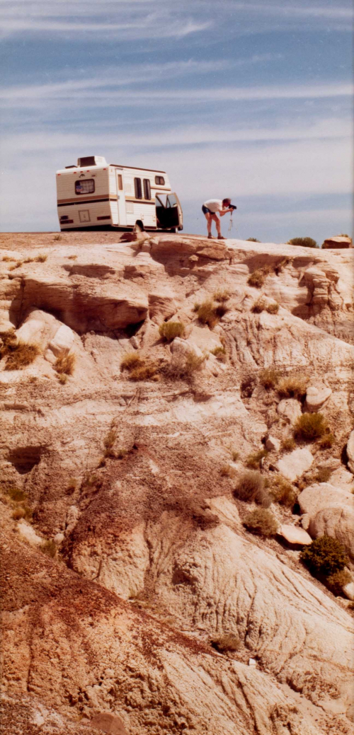 Person shooting a camera on top of a cliff, with camper in the background