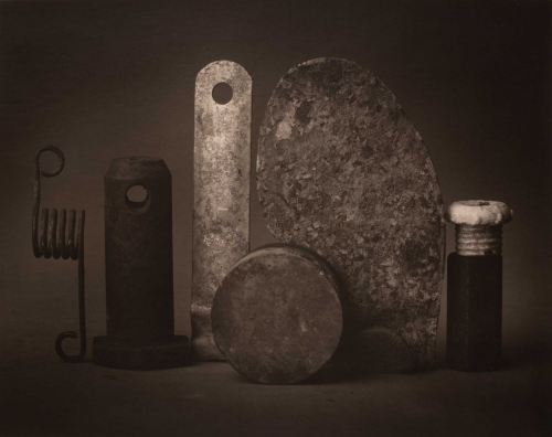 Still life of metal objects aligned horizontally along lower edge.  Five objects are placed vertically across plane