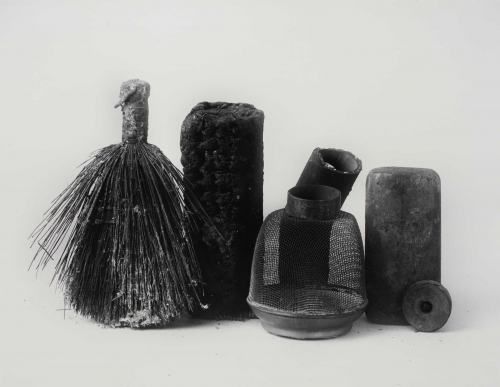 Still life of textured objects aligned horizontally. Still life includes, from left to right: small whiskbroom, wire-mesh object