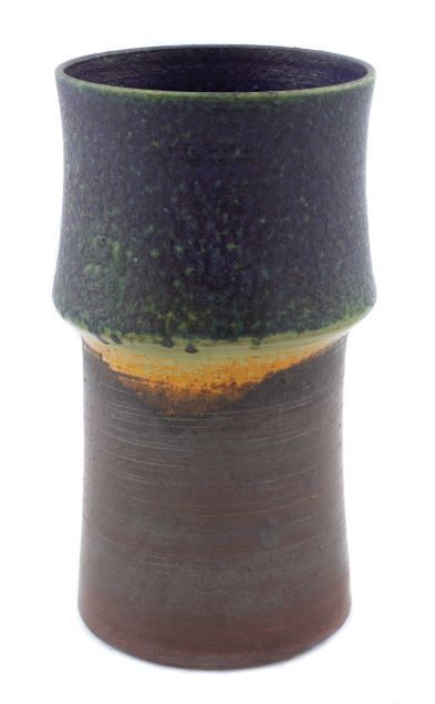Dark, cylinder with a widened ridge at the middle of the piece, brown, yellow, and green glazing
