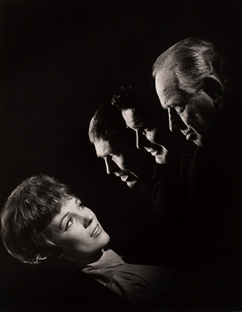 Woman's face and shoulders emerging from black background from lower left. three faces of men at angle from mid right