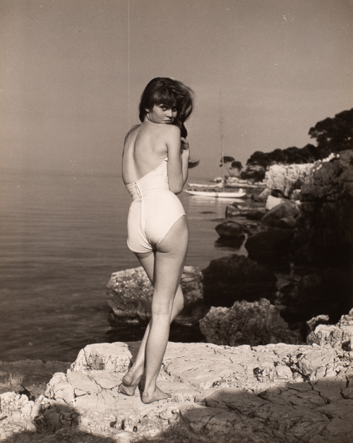Full view of woman in bathing suit with back to viewer  standing on a rock. Her head is turned to look back over shoulder
