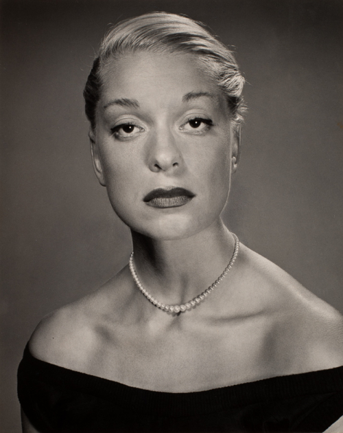 Bust of woman facing viewer directly wearing black dress with portrait collar and a pearl necklace.  Her eyes are half-closed 