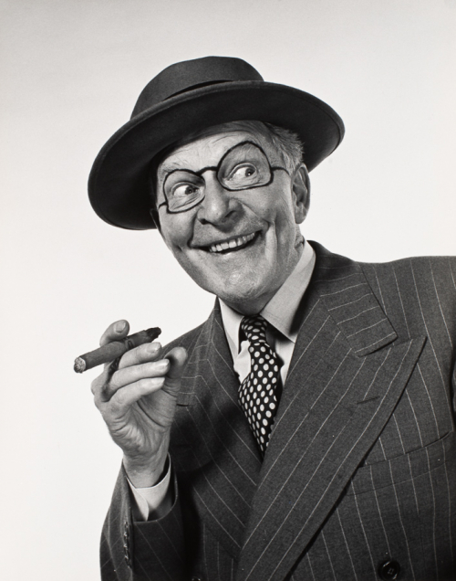 Bust of man facing viewer and wearing a pin-striped suit polka-dotted tie, and hat. glasses drawn around his eyes, holding cigar
