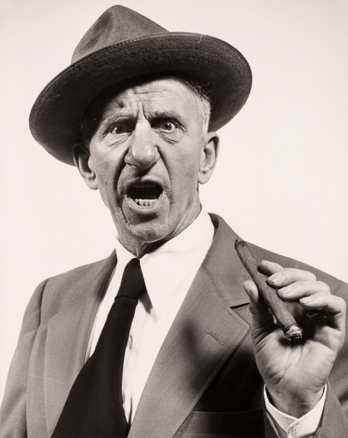 Man wearing suite and hat with angry open mouthed facial expression holding cigar