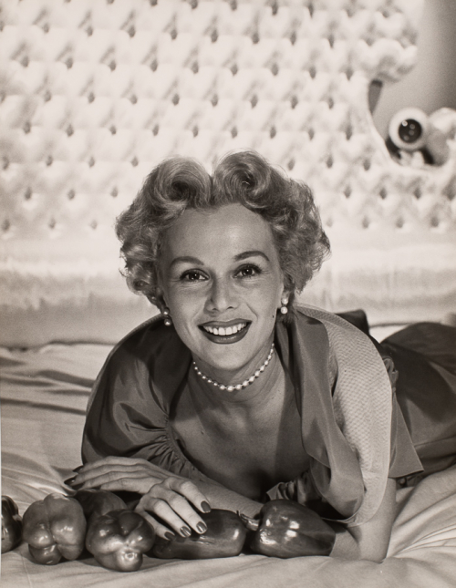 Woman with curled up-do and pearls reclining and lifted on elbows with peppers placed out in front of her