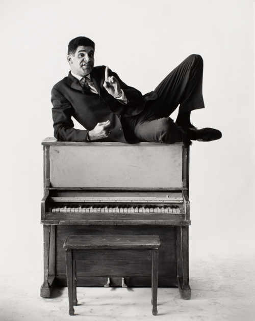 man reclining on top of a piano at center of image.