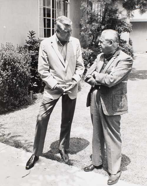  two men standing on a lawn with wall of a house to the left and back of the image