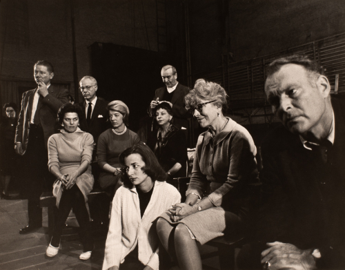 Group of people, mostly seated, seen from far right.  They are in a large room, probably on a stage. 