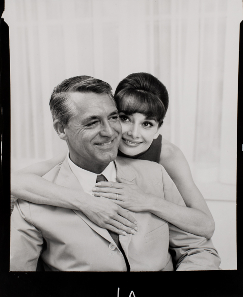 Audrey Hepburn shown embracing Cary Grant from behind, from chest up. Audrey's body his hidden behind Grant