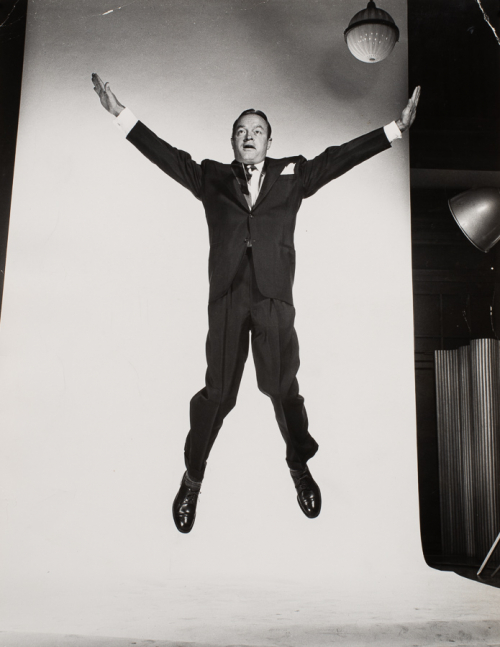 Man in suit in mid jump in front of white backdrop in photo studio, arms and legs extended outward