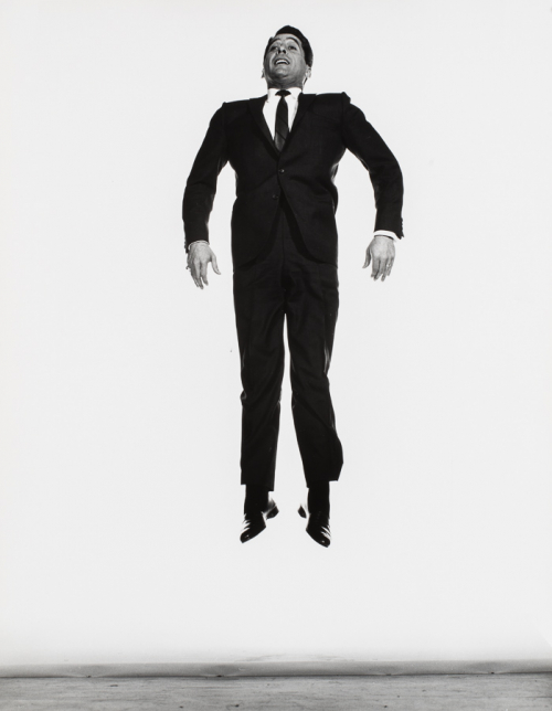 Man in suit in mid jump in front of white background, body in stiff position 