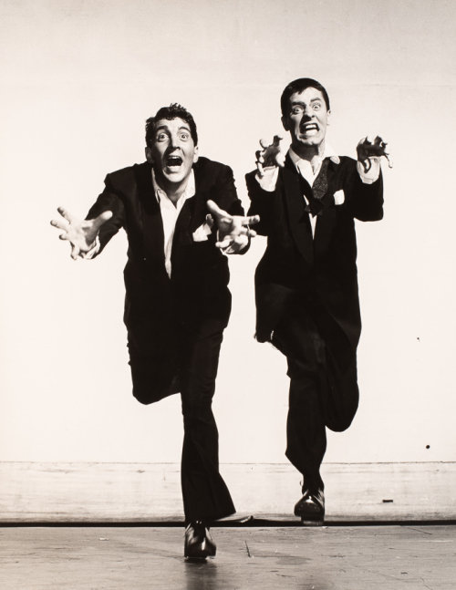 Jerry Lewis and Dean Martin in a running like motion at viewer making faces and holding hands in front