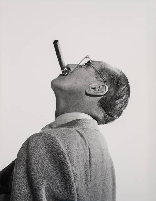 Man with back tilted turned slightly away from viewer to the left of the image head tilted up in profile with cigar in mouth