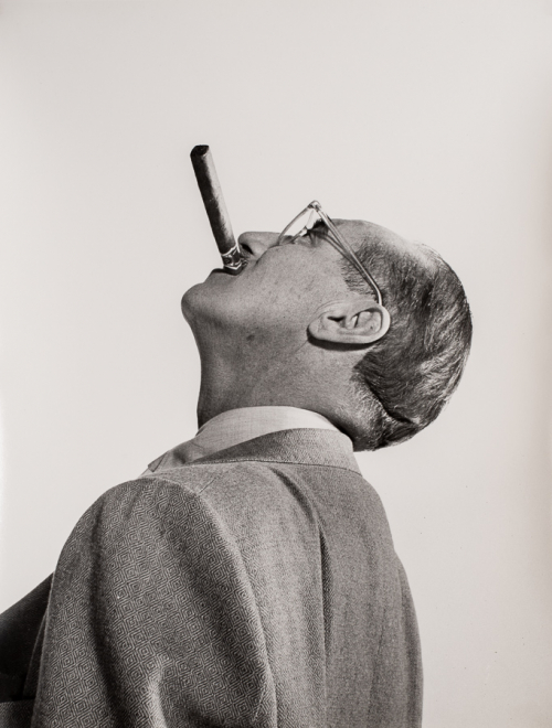 Bust-shot of man with head in left profile and tilted back, looking directly up with cigar in his mouth. Back turned to viewer.