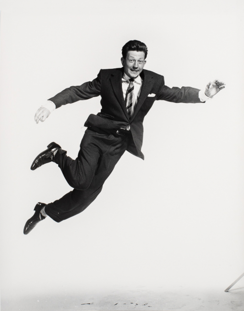 Man in suit in mid jump leaning from left of image to right of image arms and legs ben and extended 