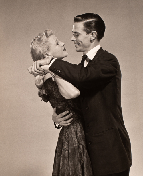 Couple embraced in a dance at center - a man wearing a suit and a light haired woman in dark dress