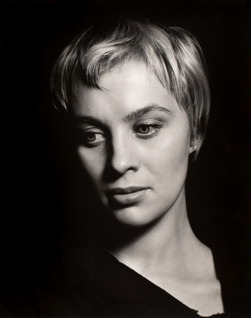woman with short blonde hair from shoulders up emerging from black background 
