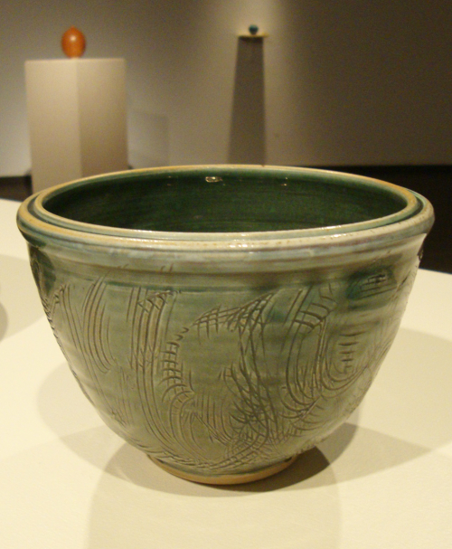 A bowl form with a small foot and indented rim, incised with curvilinear markings and glazed in celadon green