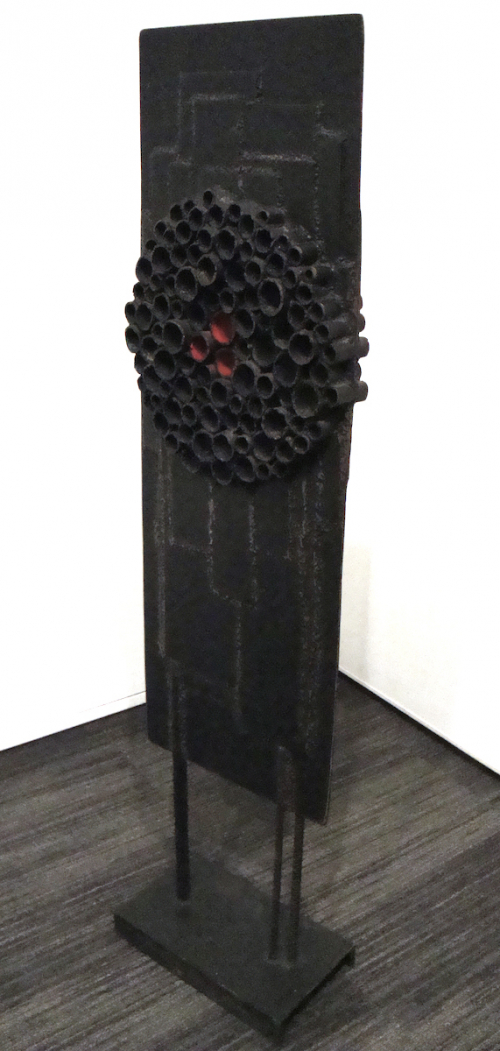 A tall narrow black sculpture puncuated with discs, several painted red inside